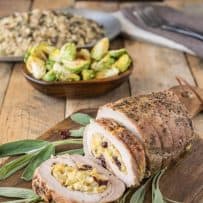 Cornbread apple cranberry stuffed pork loin sliced on a board with fresh sage