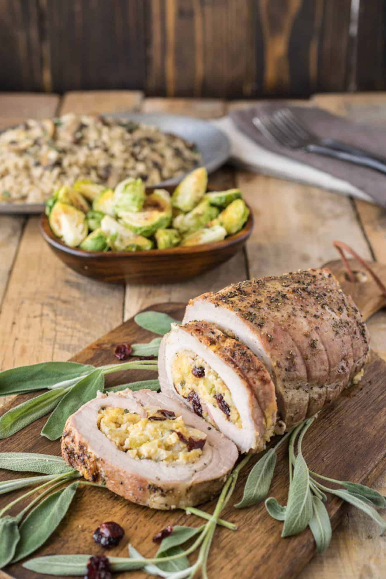 Cornbread apple cranberry stuffed pork loin sliced on a board with fresh sage