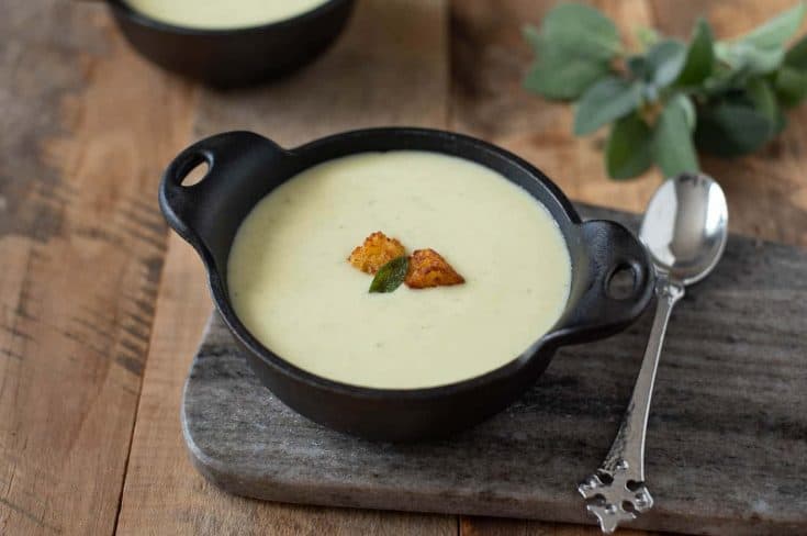 A bowl of cornbread, sage and onion soup on a serving platter with a spoon