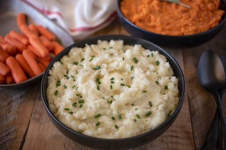 Creamy microwave mashed potatoes in a black bowl topped with chives, carrots and mashed sweet potato