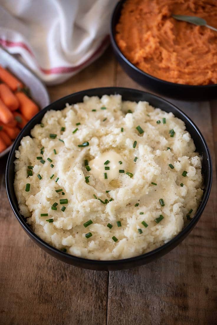 Mashed potato in a black bowl garnished with melted butter and chopped chives