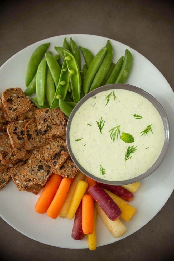 Colorful carrots, fig crackers and snap peas arranged on a plate with dipping sauce viewed from overhead