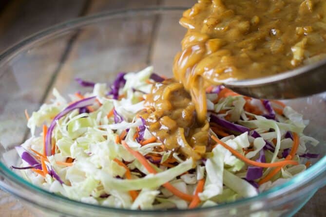 Pouring a cooked vinaigrette over shredded coleslaw mix.