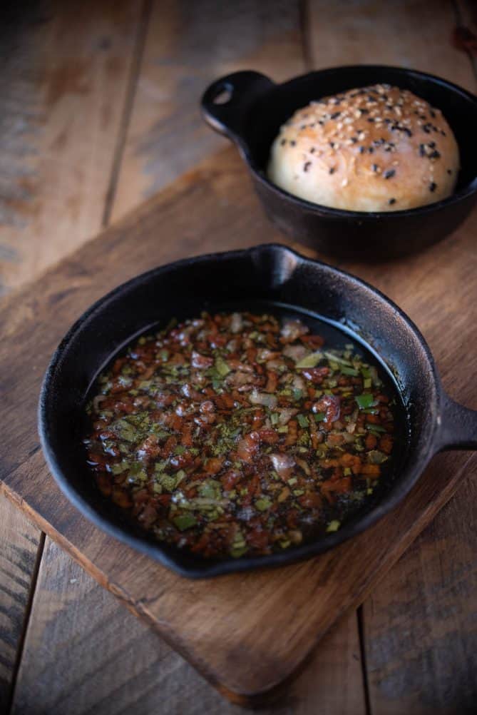 Melted butter, bacon and sage in a mini cast iron skillet with a bread roll in the background