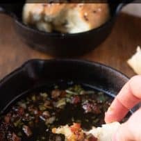 A piece of crusty bread roll scooping up bacon bits with sage and melted butter