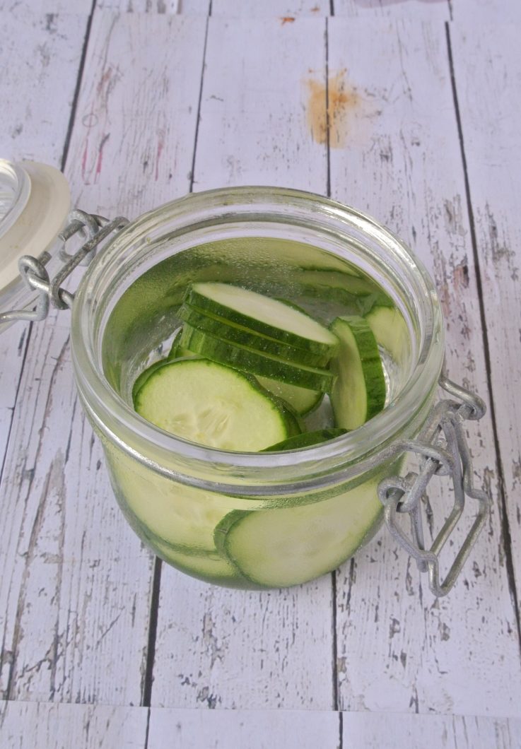 A jar of gin being infused with fresh cucumbers