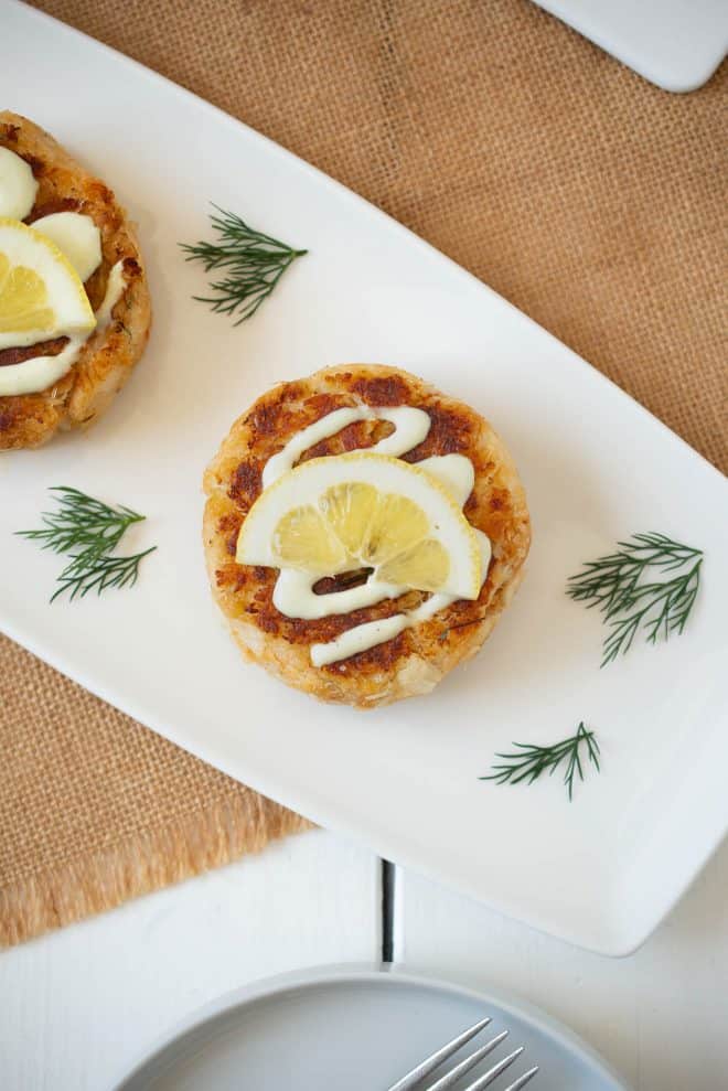 Crab cake viewed from overhead topped with sauce and a lemon slice