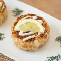 A Dungeness crab cake on a plate with sauce, lemon and dill