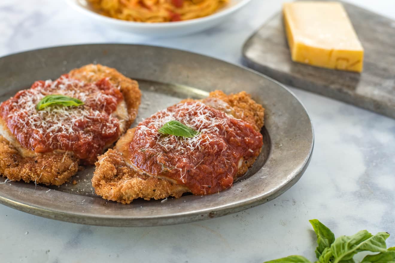 2 breaded and fried chicken breasts topped with marinara sauce and cheese with fresh basil