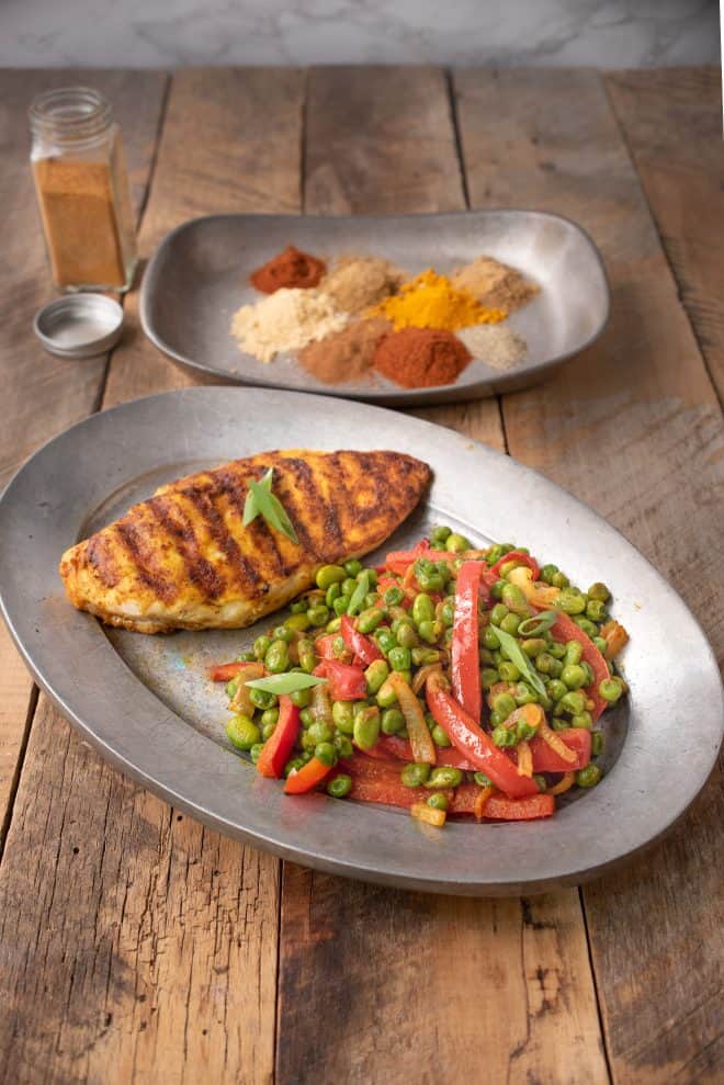 A oval plate with a grilled chicken breast with Indian spices peas