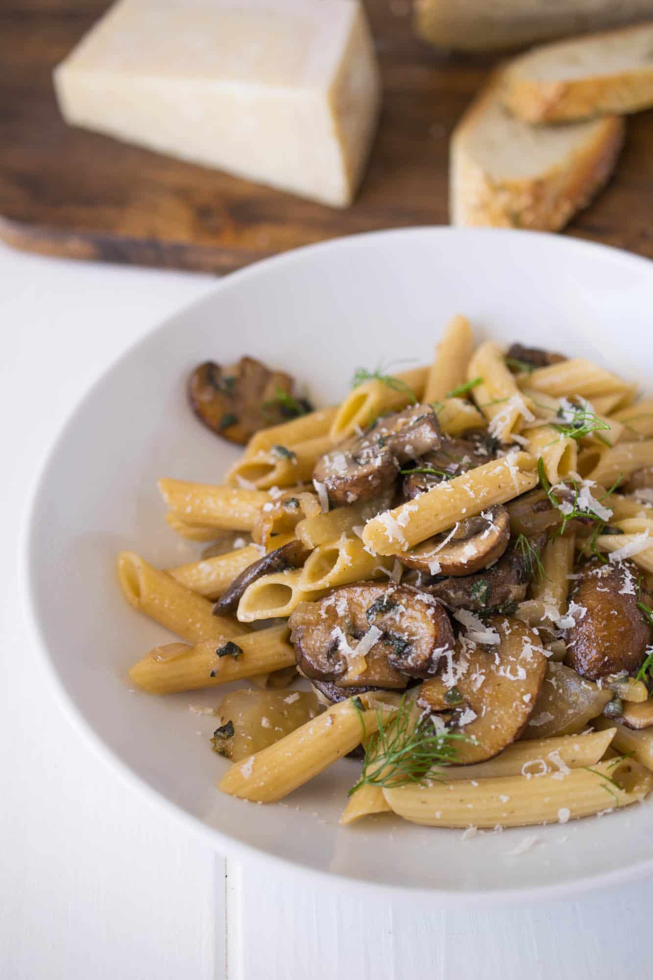 Easy mushroom, fennel & sage pasta in a white bowl with crusty bread and Parmesan cheese