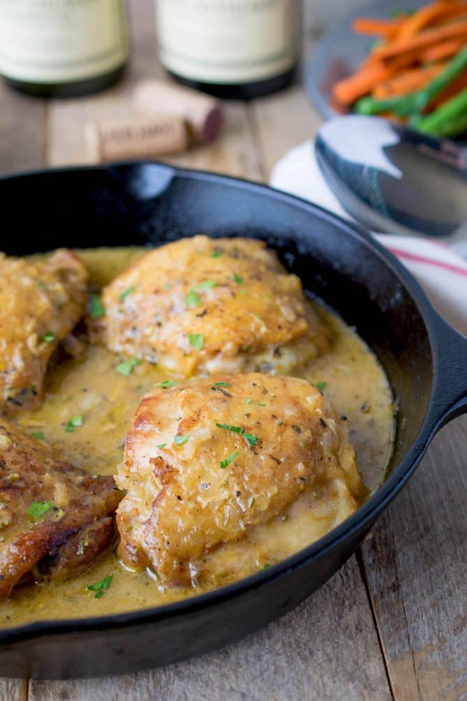 A cast iron skillet cooking up 4 chicken thighs in a Dijon sauce