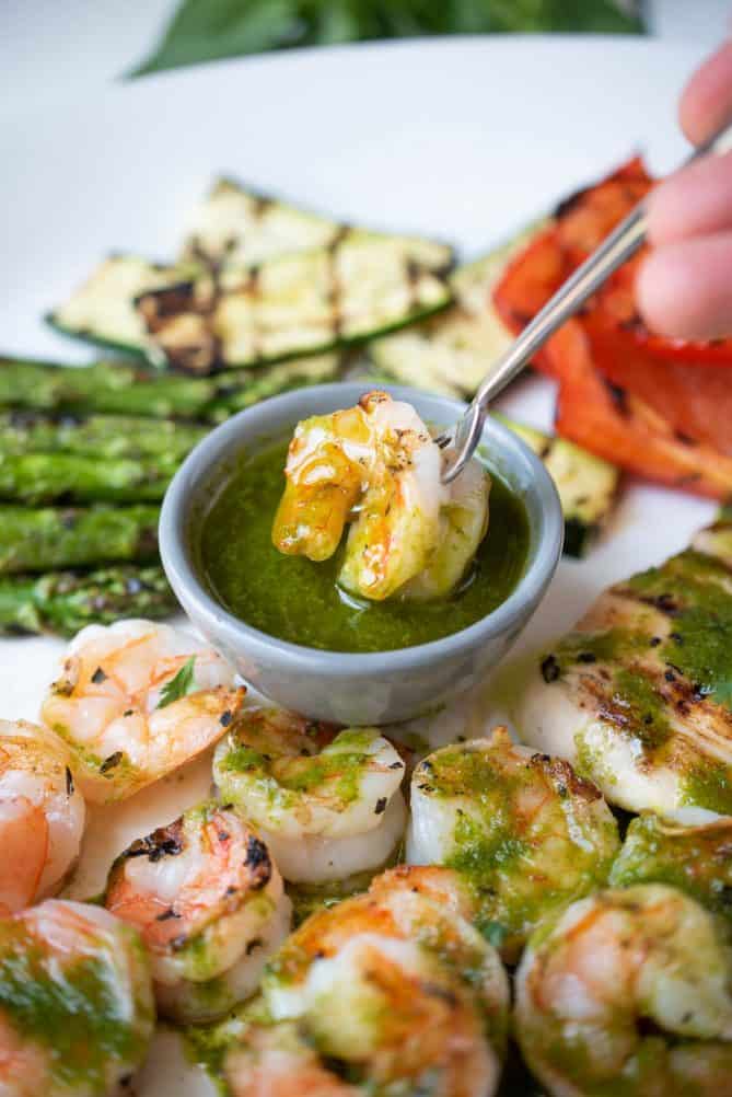 Dipping a grilled shrimp into a bowl of herb sauce