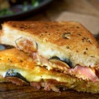 Flecks of rosemary on the bread of a grilled cheese sandwich with fig and prosciutto cut in half