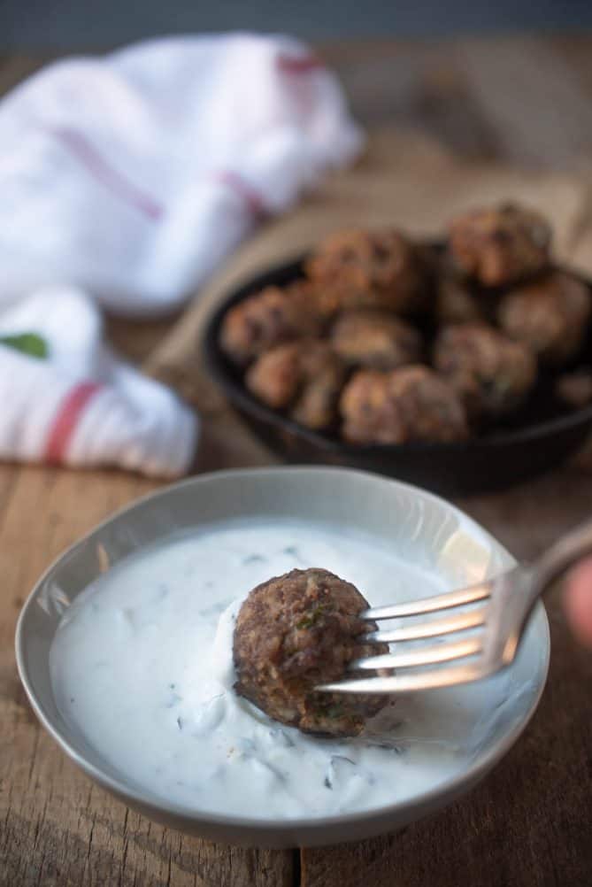 Dipping a meatball into a white yogurt sauce