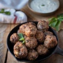 A cast iron skillet filled with Greek meatballs garnished with fresh mint leaves