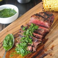 Grilled filet mignon with mint and parsley served on a cutting board with grilled corn on the cob