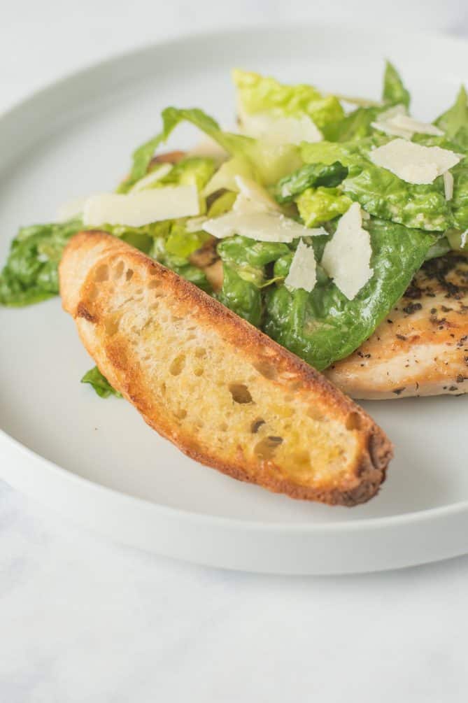 A large, toasted crouton propped up against lettuce with Parmesan and chicken