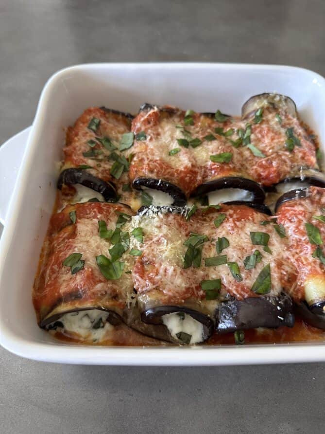 A closeup of eggplant rollatini rolls in a white baking dish