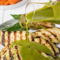 Chicken breasts with grill marks with herb sauce being poured over