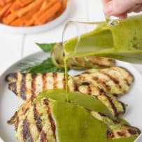 Pouring herb sauce over grilled chicken breasts