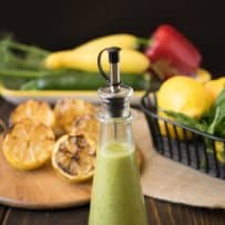 A salad dressing bottle filled with dressing with grilled lemons in the background