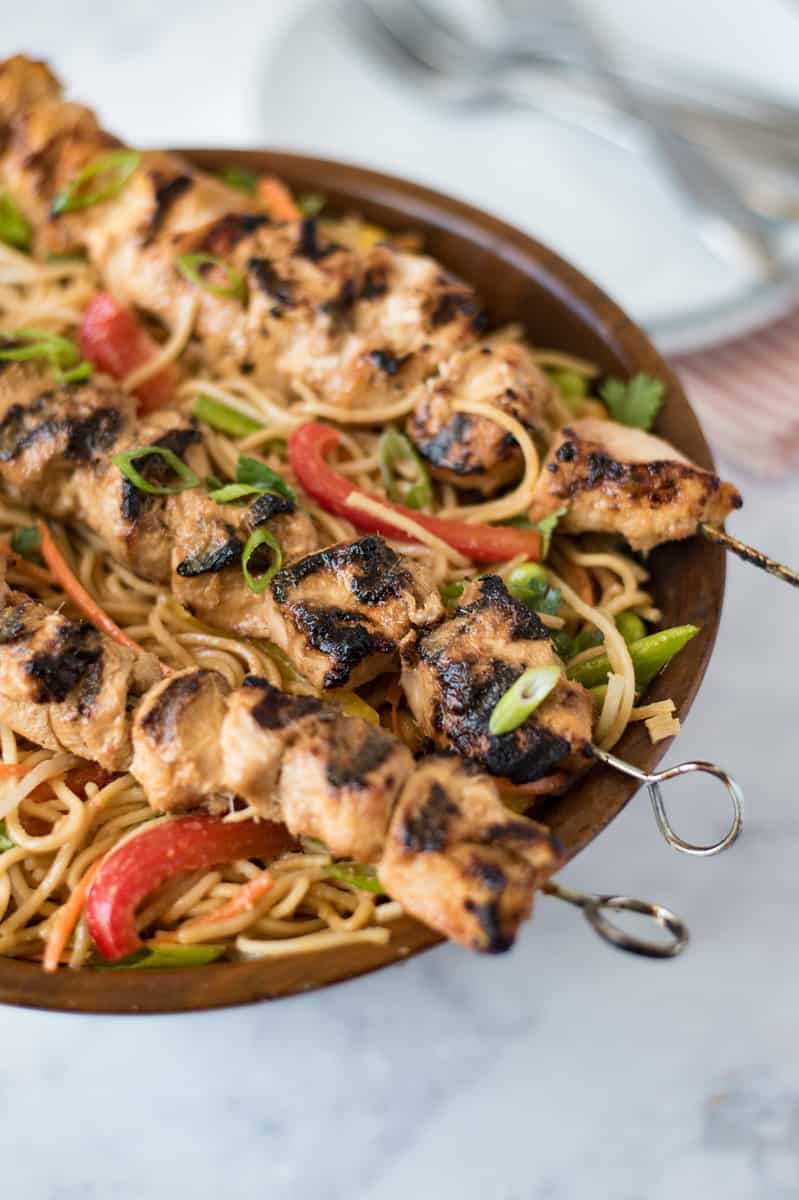 A large bowl of lemongrass noodle salad with lemongrass grilled chicken skewers laid across the top