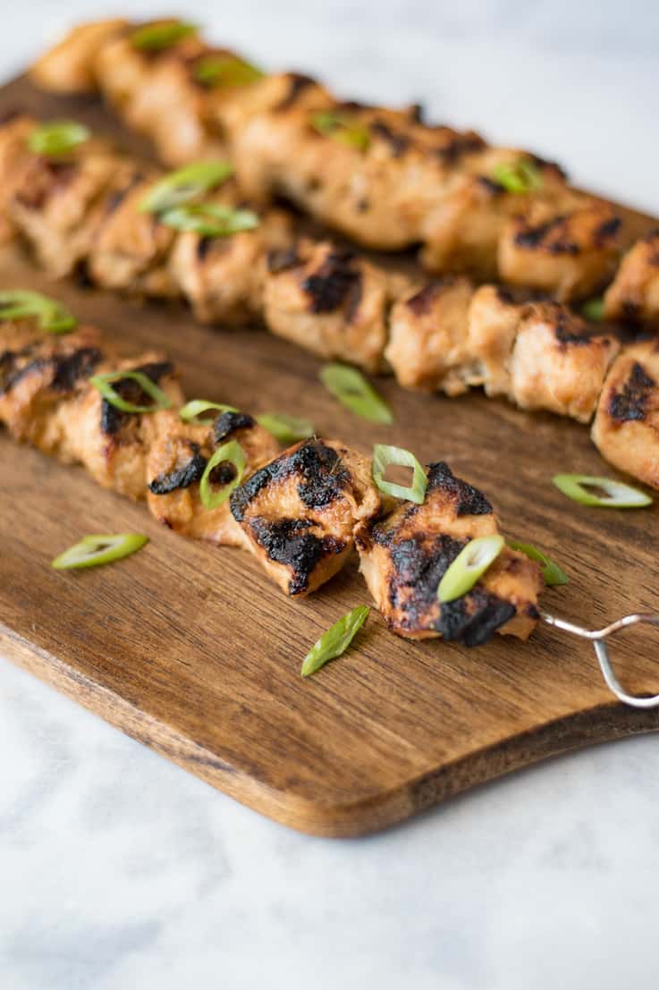 Grilled lemongrass chicken skewers on a serving board garnished with sliced scallions