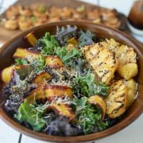 Slices of grilled pineapple on a bed of kale with shaved carrot and toasted coconut