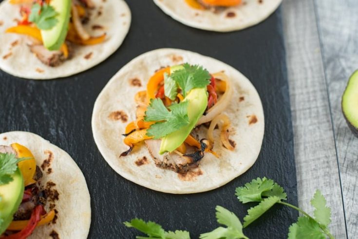 Grilled pork tenderloin fajitas are a quick and easy way to get a summer meal served in under 30 minutes. Marinated pork tenderloin is grilled along with onions and peppers. The pork is sliced then all are served on warm tortillas garnished with fresh avocado and cilantro.