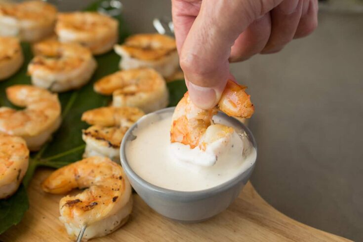 dipping a grilled shrimp into a white sauce