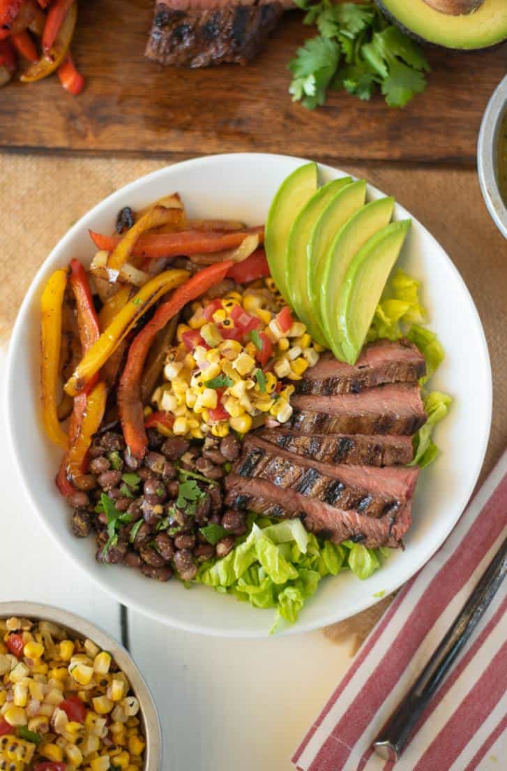 An assembled fajita bowl overhead image in a white bowl with a fork and garnishes