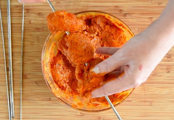 Chicken being threaded onto metal skewers