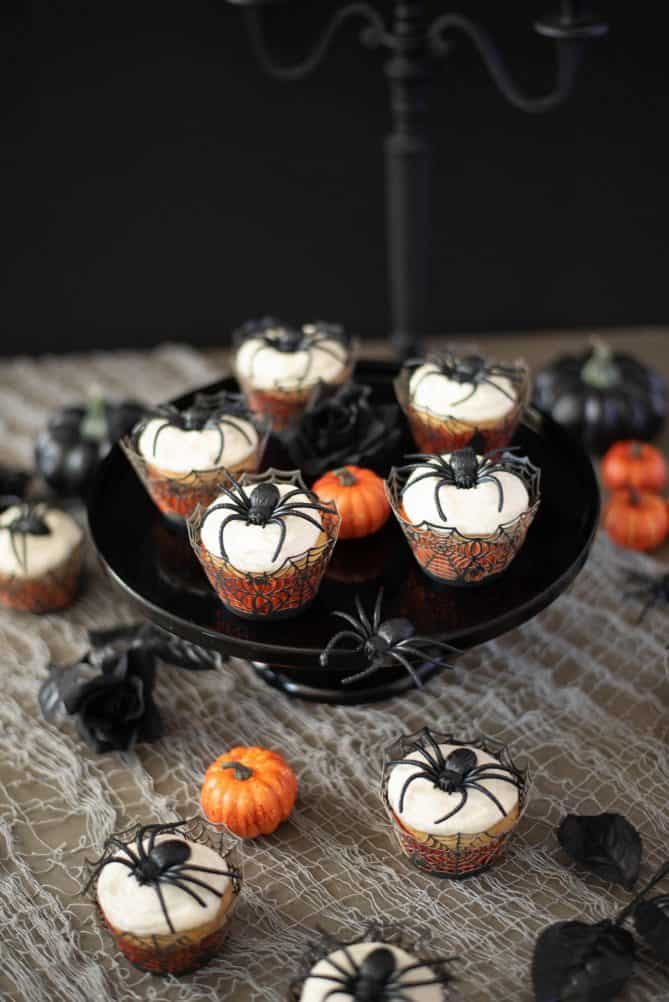 5 spider cupcakes on a black cake stand with some cupcakes underneath