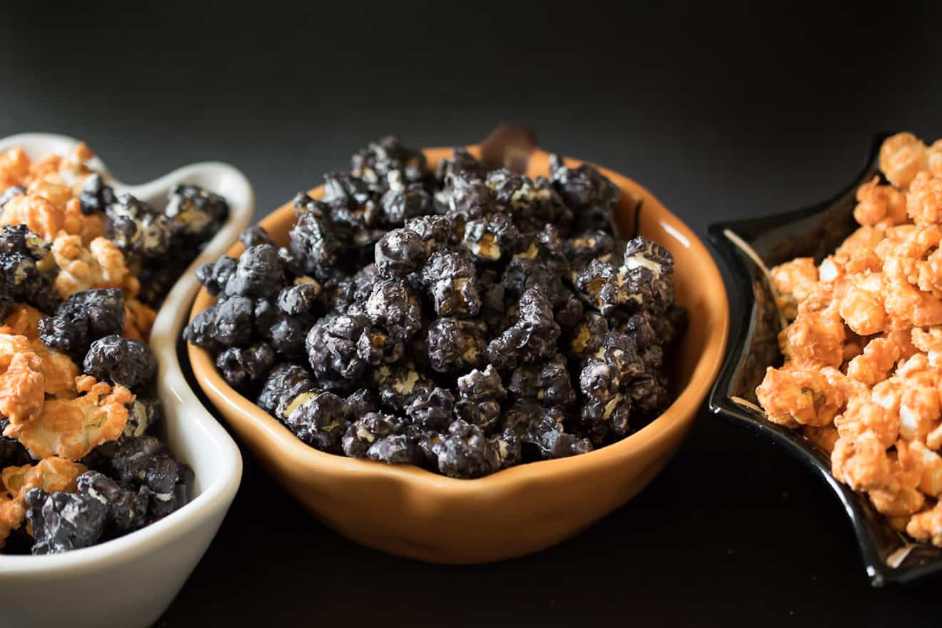 An orange pumpkin bowl filled with black popcorn