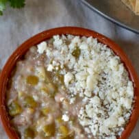From scratch refried beans cooked with hatch Chile peppers served in a clay bowl topped with crumbled queso fresco cheese