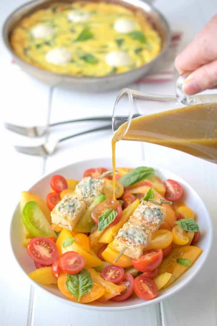 Pouring dressing over colorful heirloom tomatoes with fresh basil and croutons