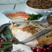 Carving slices of a roast turkey breast with carrots in the background and a sweet potato casserole