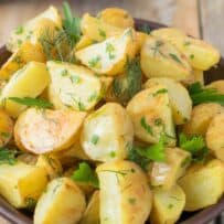 A closeup of potato wedges in potato salad with fresh herbs