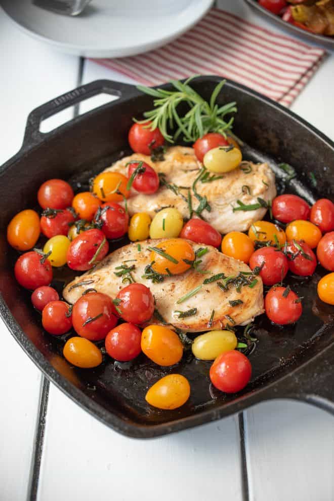 A cast iron skillet with 2 chicken breast, tomatoes and herbed butter