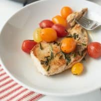 A chicken breast with herbed brown butter and tomatoes on a white plate