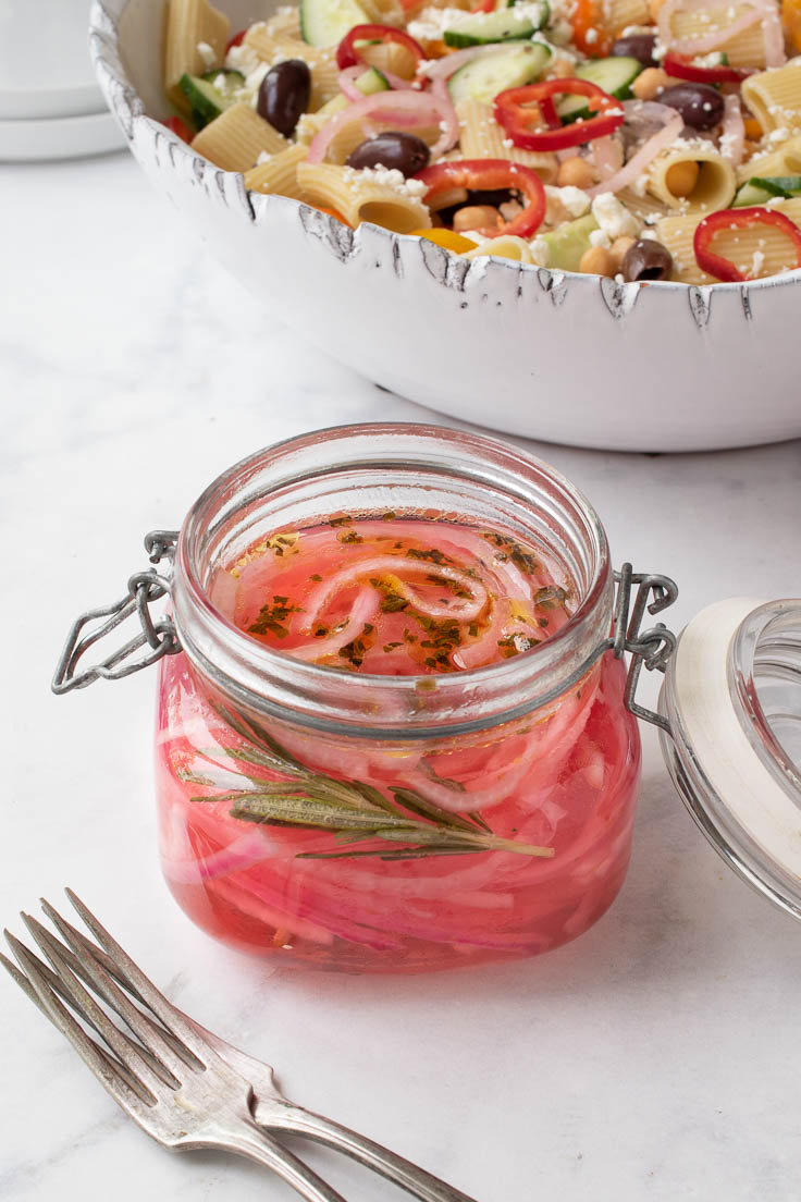A pop sealed jar filled with red onions, vinegar, herbs and garlic
