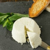 Ricotta cheese on a slate board with a knife and crusty bread