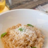 Creamy risotto in a white pasta bowl topped with basil leaves and grated Parmesan cheese