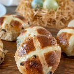 A closeup of a hot cross bun on a board with Easter eggs