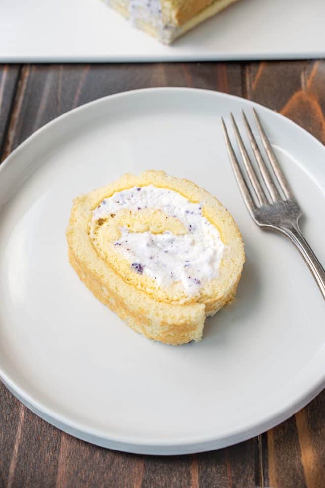 A slice of Ice Cream Swiss Roll Cake on a round white plate with a fork