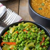 A black bowl filled with green peas with red pepper and onions
