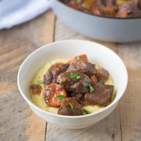 Italian beef stew served in a white bowl over creamy polenta