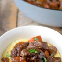 A white bowl filled with polenta topped with beef stew