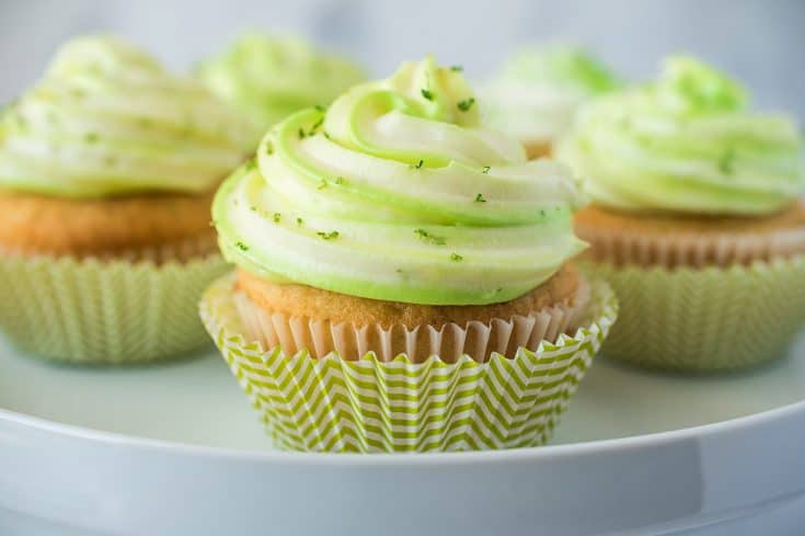Key lime cupcakes on a cake stand in green and white striped cups